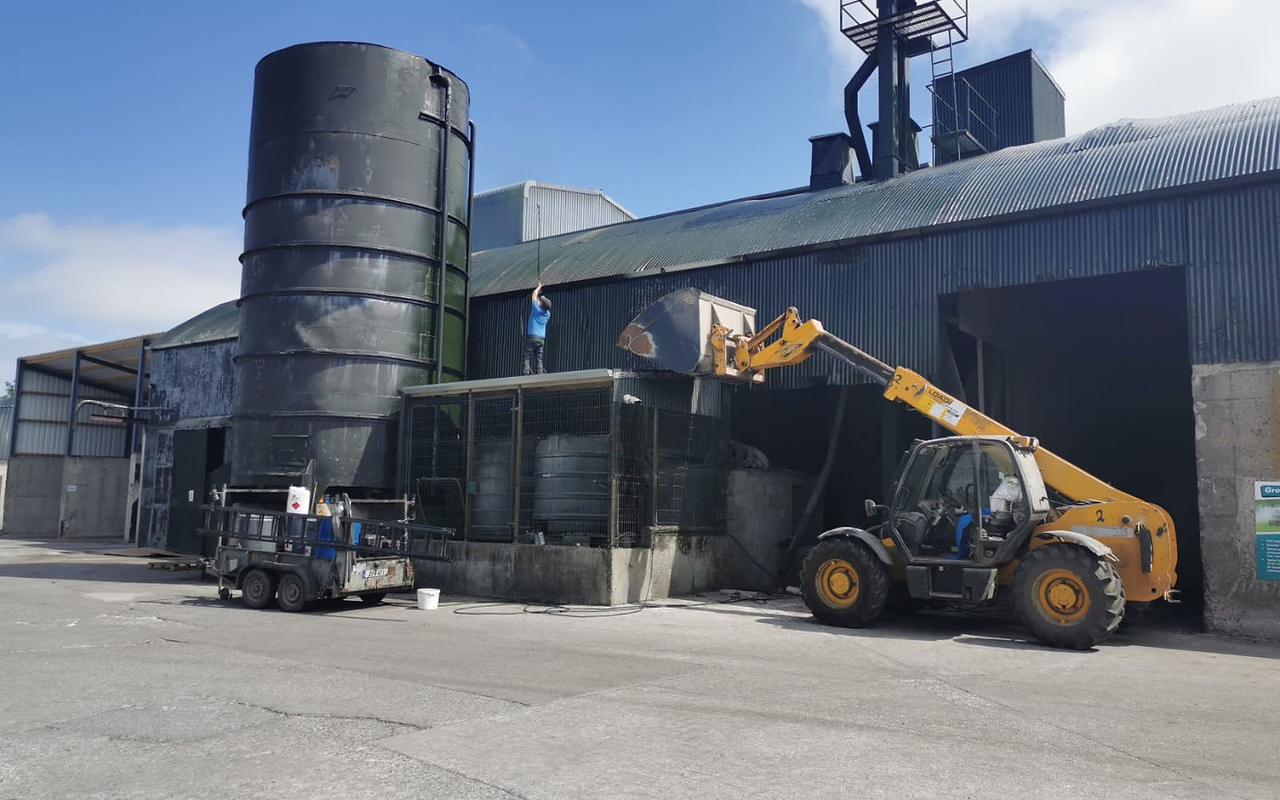 Forklift loading a structure next to a tall silo on a sunny day.