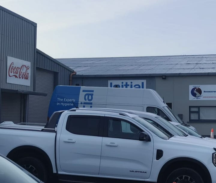 Coca-Cola sign and Initial van with other vehicles in front of buildings.